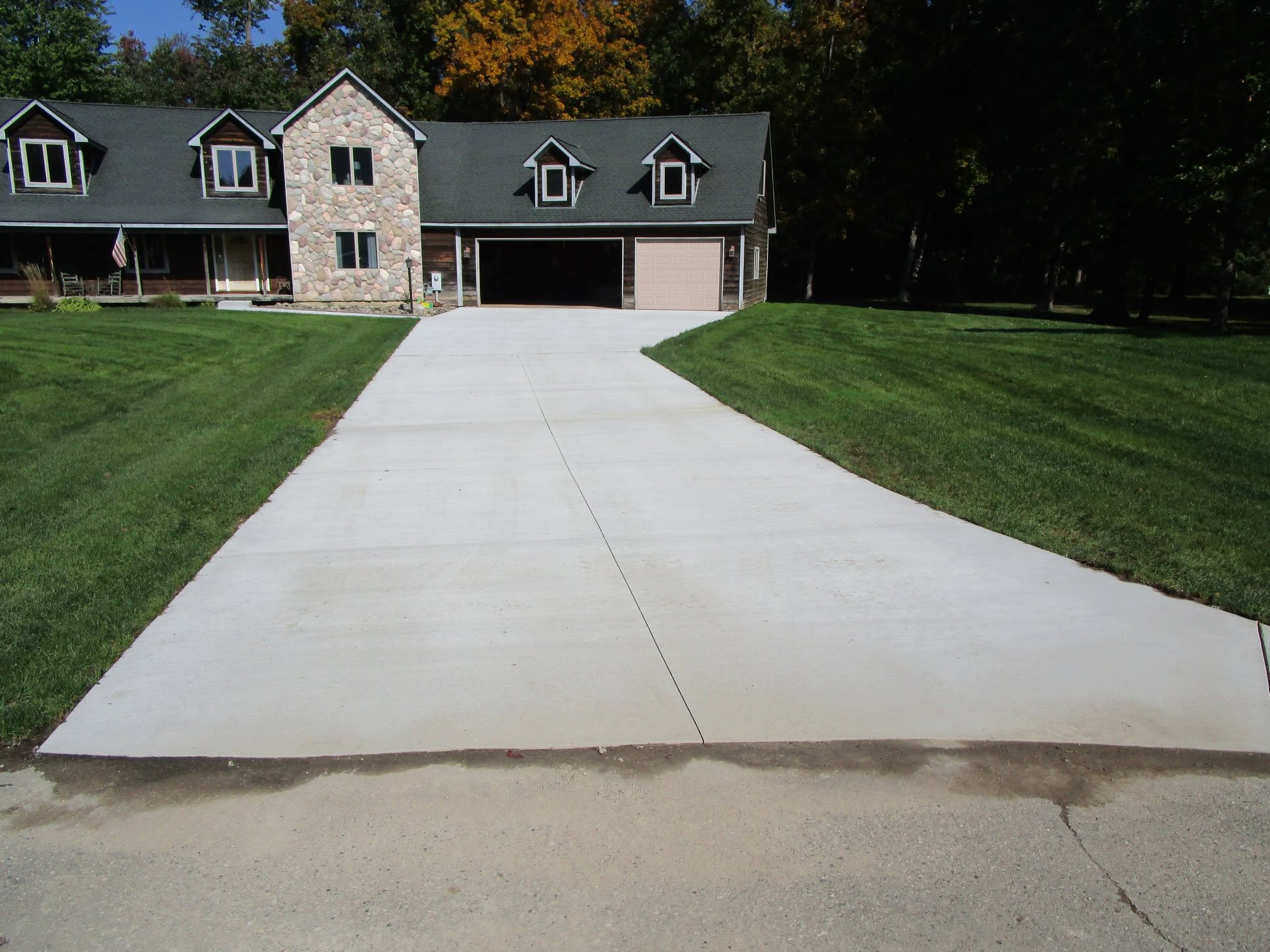 New concrete driveway with saw-cut joints leading to an attached two-car garage at a wood-and-stone home by Marcucci Concrete