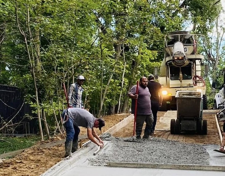 Marcucci crew pouring and finishing a concrete driveway with a ready-mix truck chute at a residential jobsite in Oakland County, Michigan